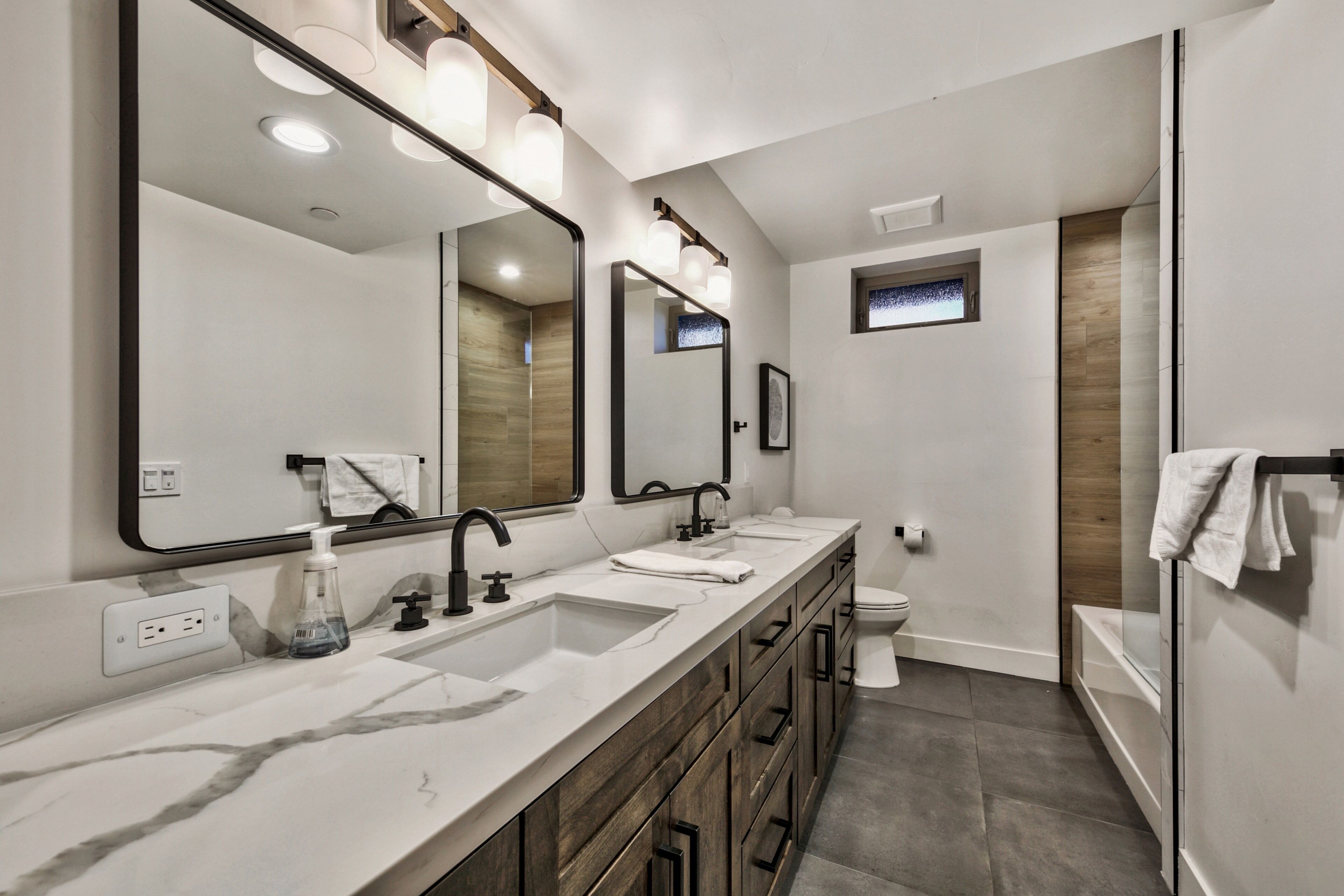 A modern bathroom with a large mirror, dual sinks, and a toilet.