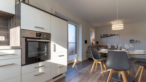 Eine moderne Küche mit integrierten Geräten, ein Essbereich mit rundem Tisch und Stühlen sowie ein großes Fenster für natürliches Licht.