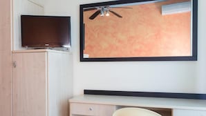 Une chambre d’hôtel avec un téléviseur posé sur un meuble, un bureau avec une chaise et un ventilateur de plafond.