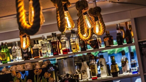 Un bar décoré de guirlandes lumineuses suspendues et doté d’étagères remplies de bouteilles d’alcool.