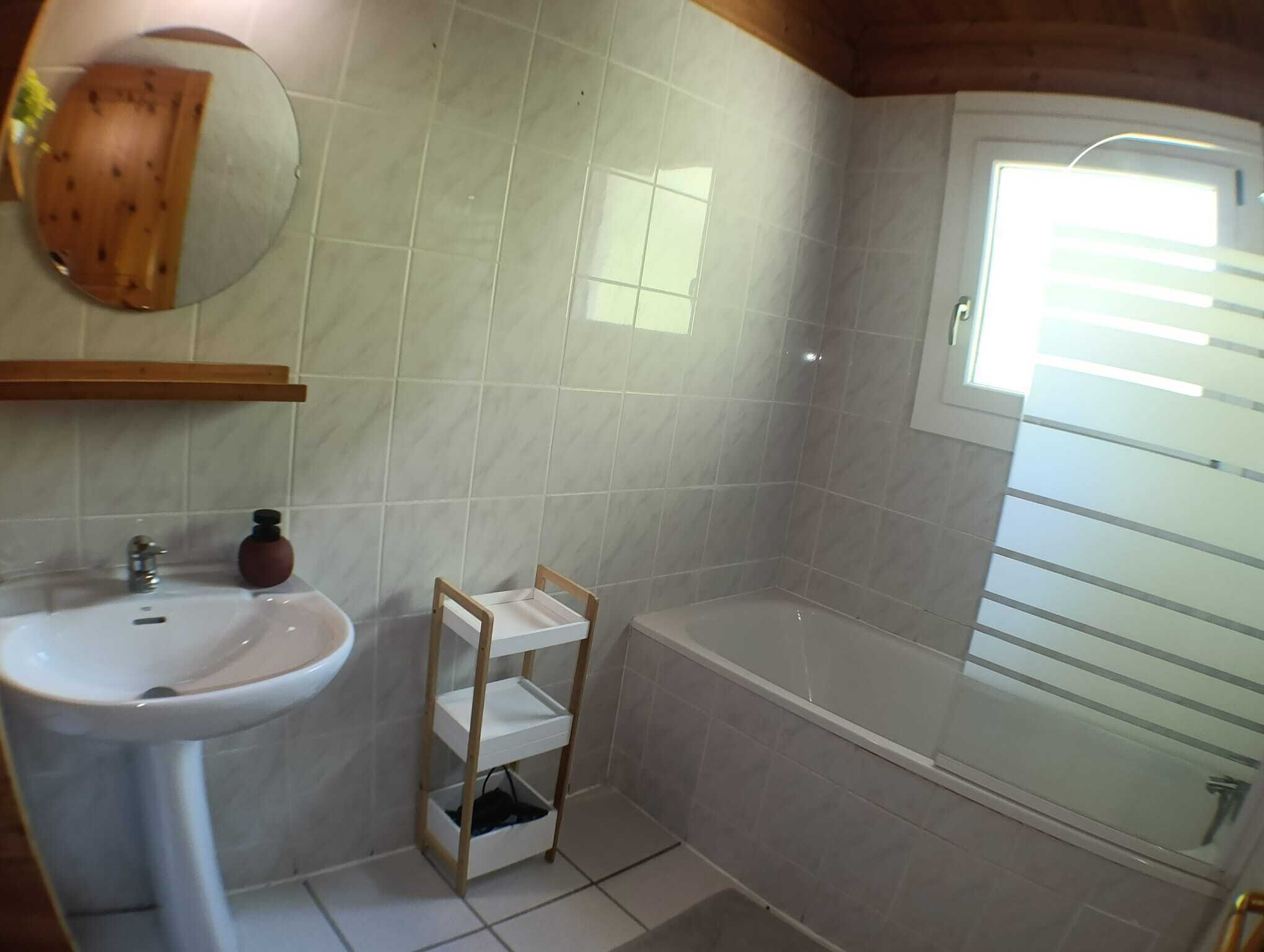 A bathroom with a white sink, a wooden shelf, a mirror, and a bathtub.