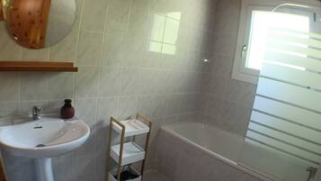 A bathroom with a white sink, a wooden shelf, a mirror, and a bathtub.