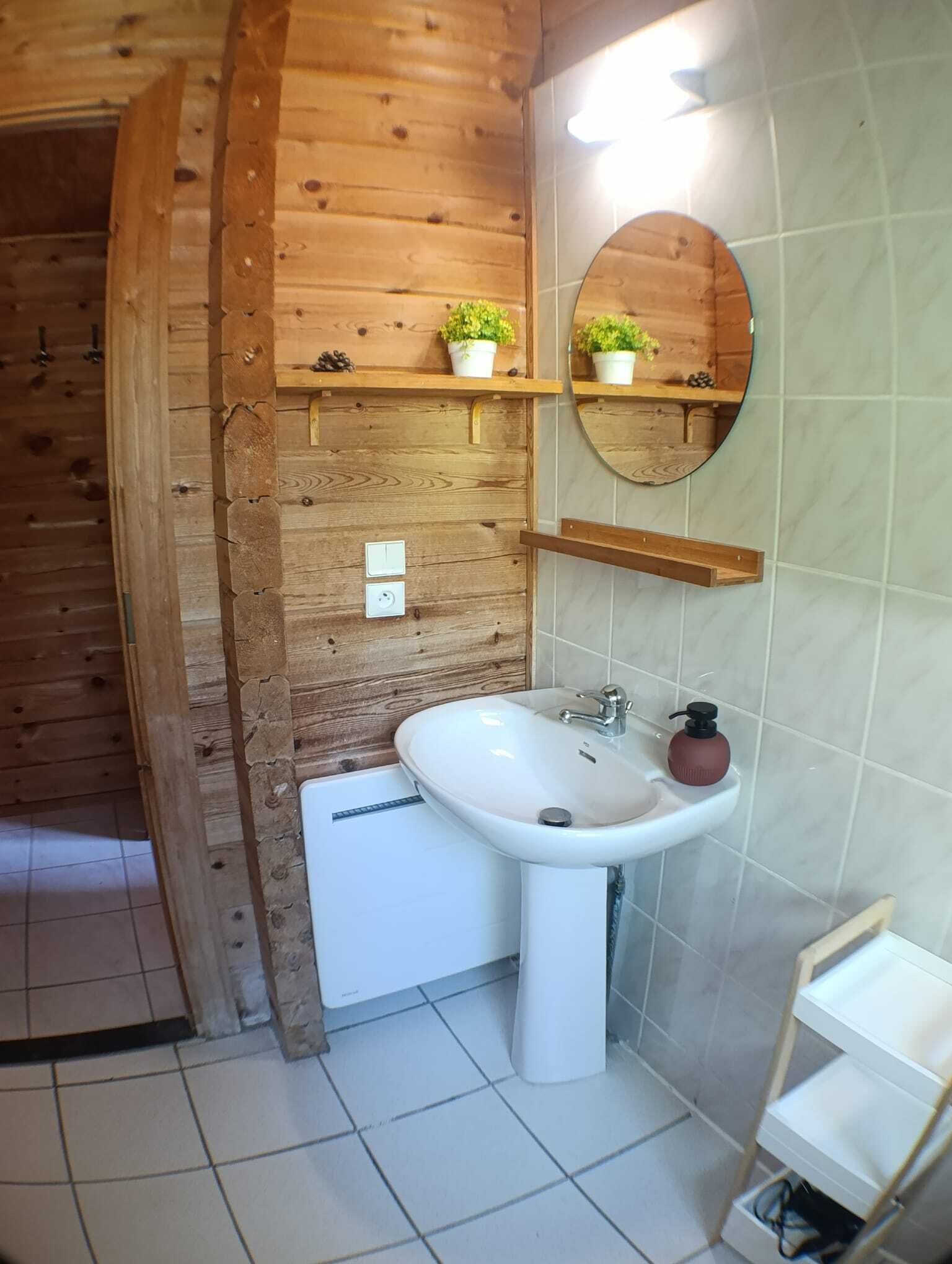 Un baño con pared de madera, un lavabo blanco, un espejo y estantes con plantas en macetas.