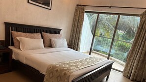 A bedroom with a bed, a nightstand, a window with curtains, and a view of greenery outside. - Silverador Resort Club (Mira Bhayandar)