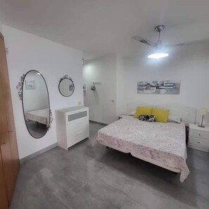 Ein Schlafzimmer mit einem Bett, einem Nachttisch, einer Kommode, einem Spiegel und einem Deckenventilator.
