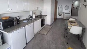 Cozinha compacta com armários brancos, micro-ondas, pia e geladeira pequena.