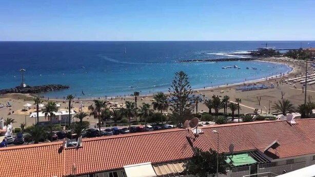 Vista costeira com praia, oceano e um edifício com telhado de telhas vermelhas.