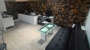 A compact living space with a stone wall, a kitchenette, a glass coffee table, and a black sofa. - Tenerife vacation home north Icod de loa Vinos La Vega view of the sea and tide (Mirabal Alto)