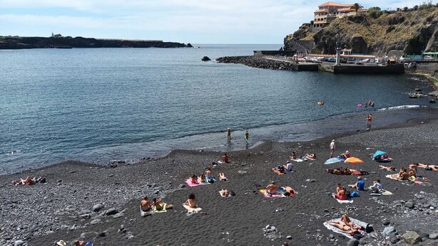 A beach with people sunbathing and swimming, a rocky shoreline, and a building on a cliff. - Tenerife vacation home north Icod de loa Vinos La Vega view of the sea and tide (Mirabal Alto)