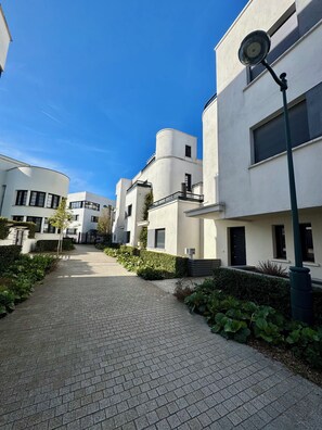 A residential street with modern white buildings, a paved walkway, and a street lamp.