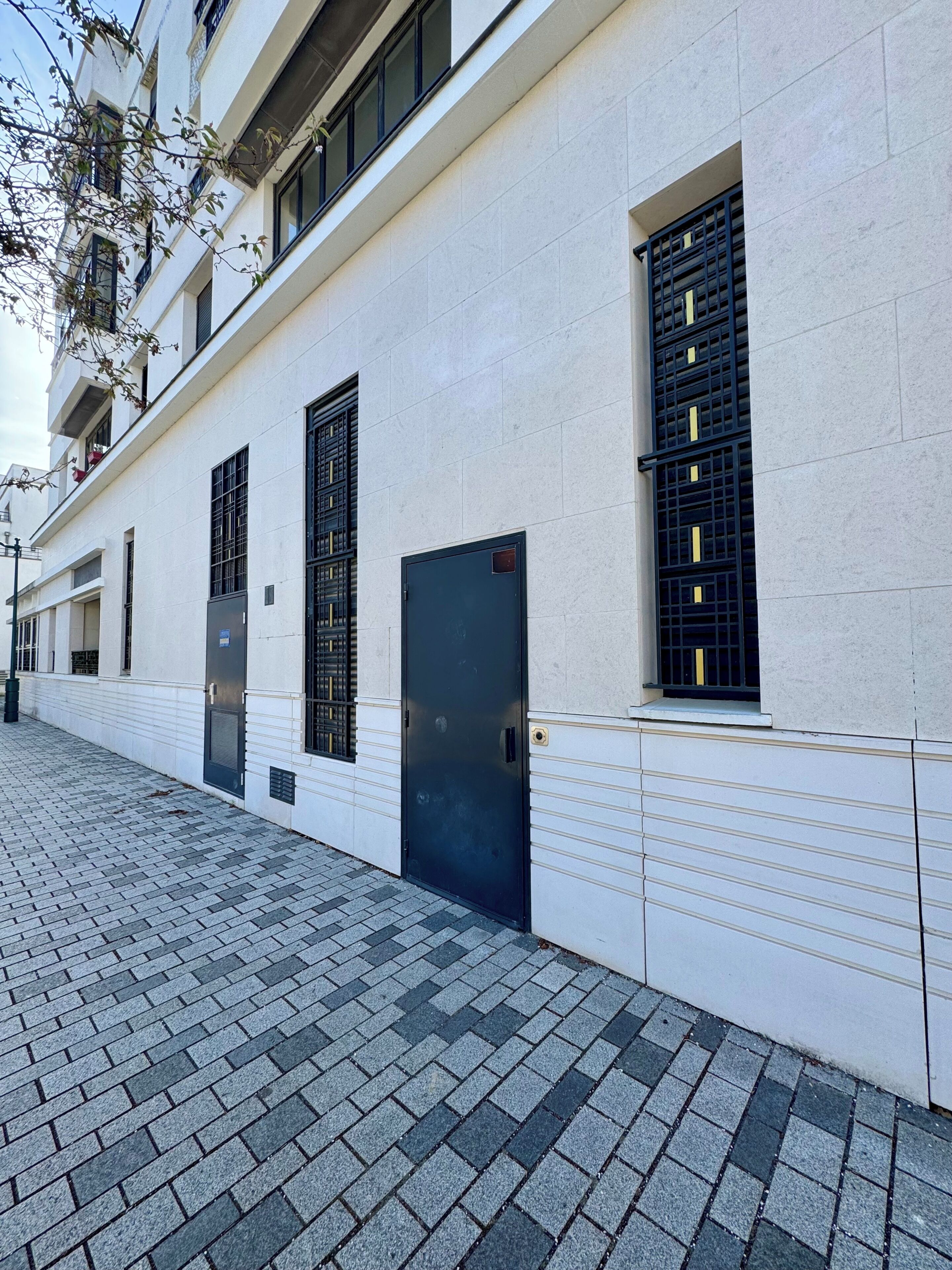 A building facade with a white exterior, multiple windows with black grills, and a paved walkway.