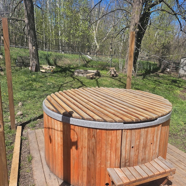 Un bain à remous en bois, doté d’un banc, entouré d’une zone herbeuse et d’arbres.
