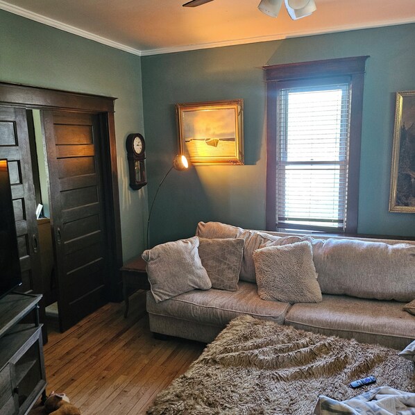 A room with a wooden door, a sofa, a lamp, a painting, and a window.