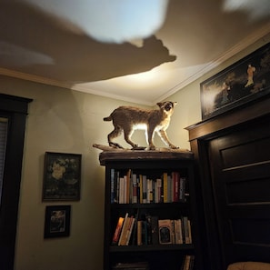 Une pièce avec une bibliothèque, un tableau et une statuette de chat posée sur le dessus.