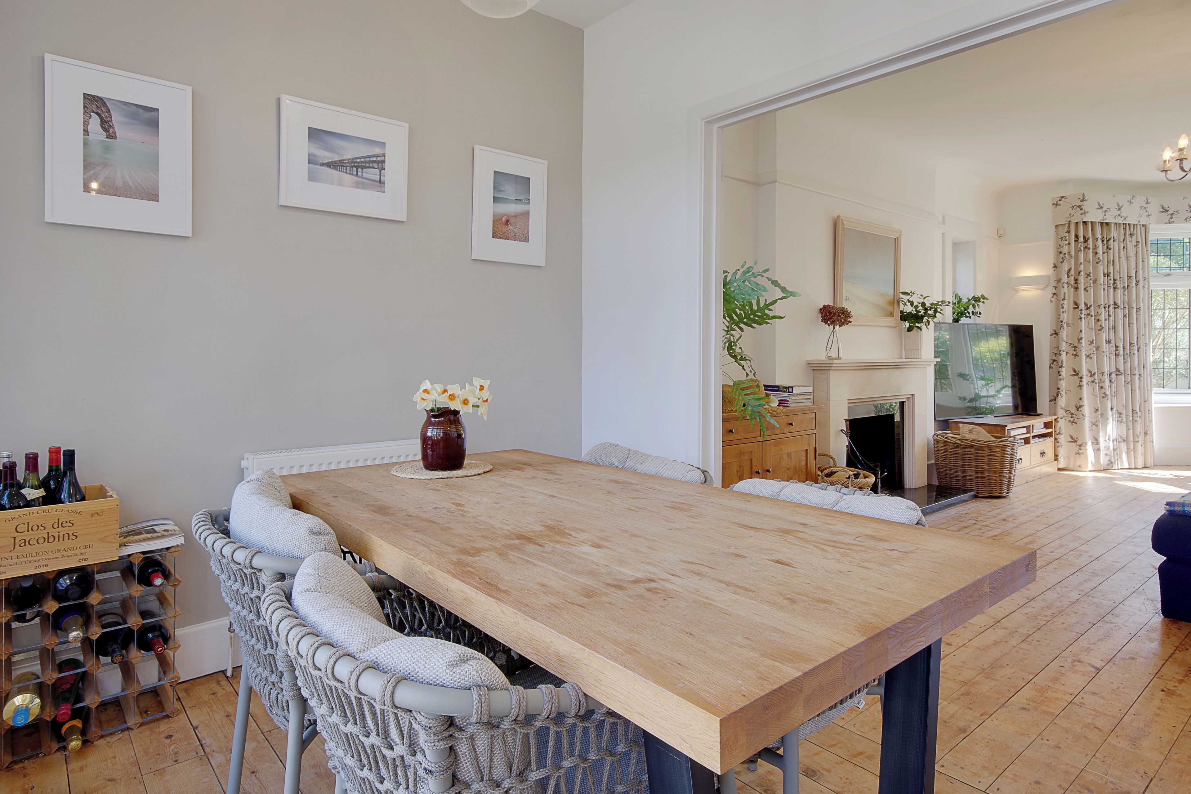 A dining area with a wooden table, cushioned chairs, a wine rack, and framed pictures on the wall.