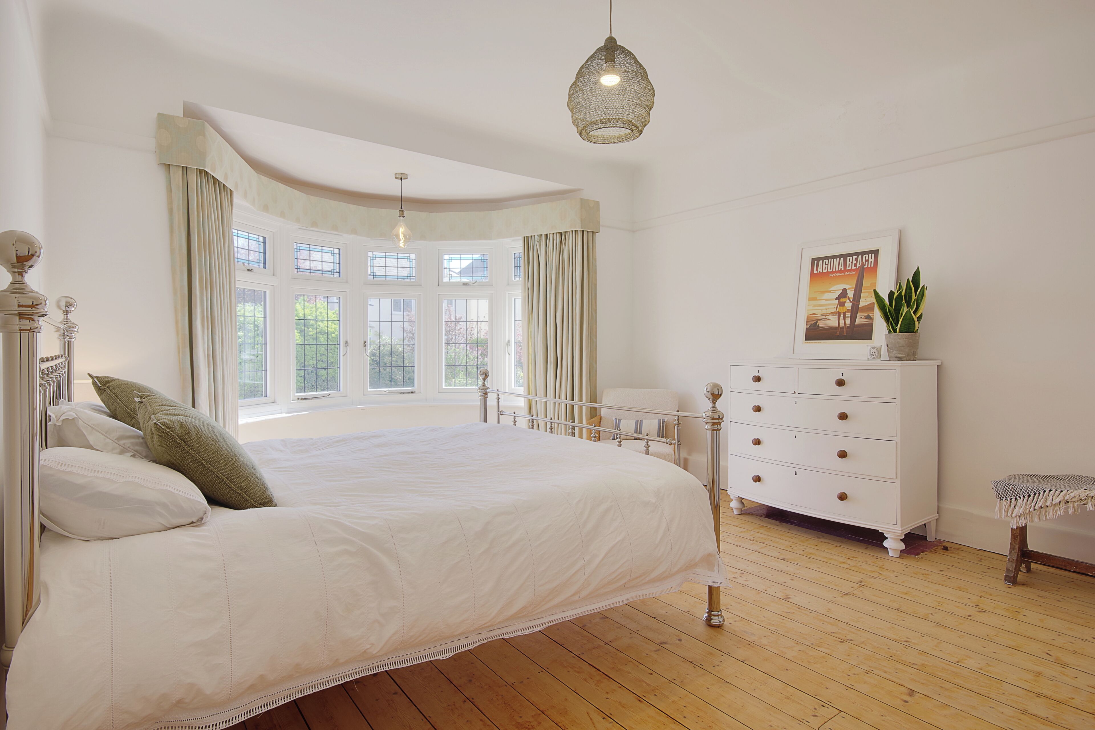 A bedroom with a large bed, a dresser, a window with curtains, and a hanging light fixture.