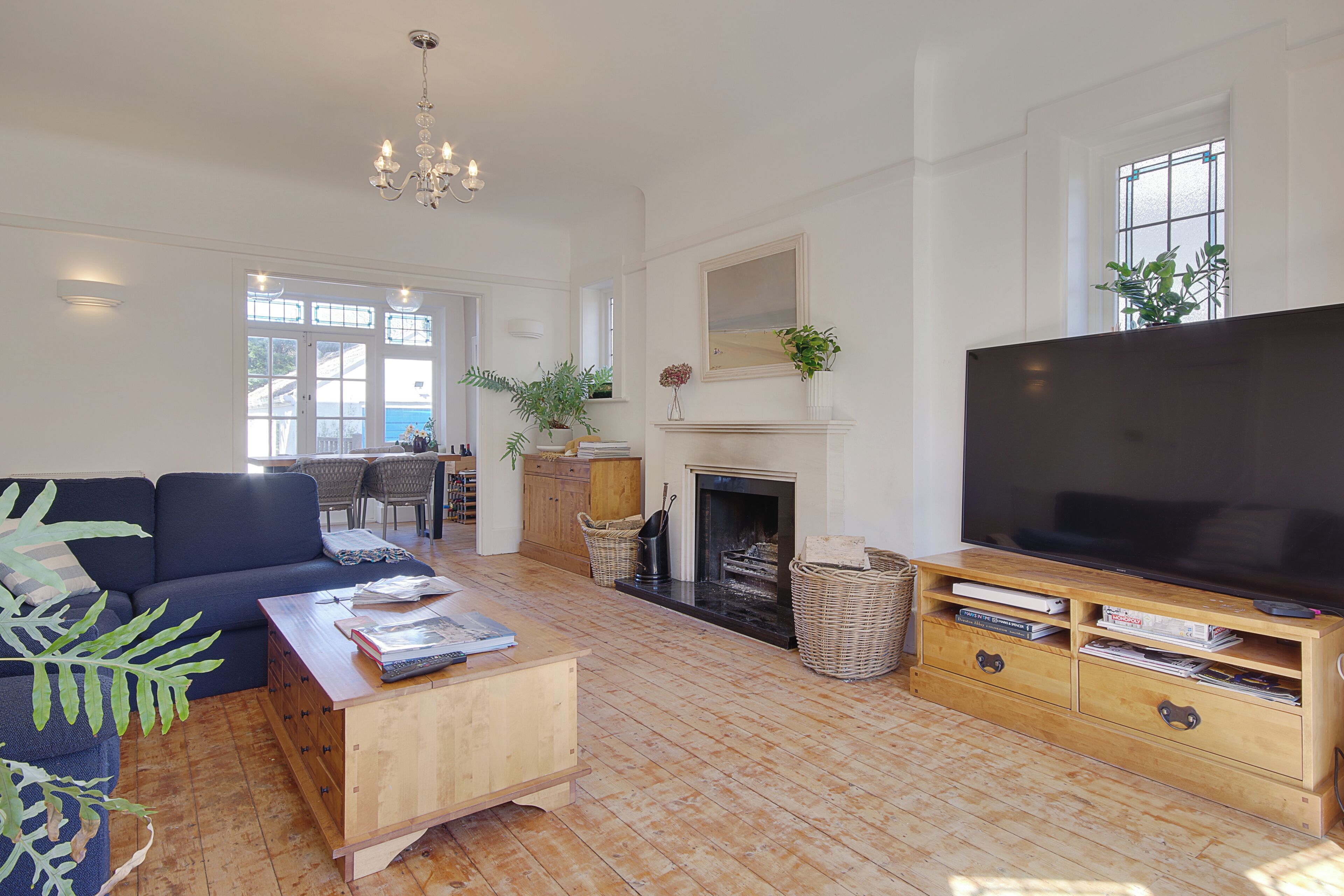 A spacious living room with a large TV, wooden furniture, a fireplace, and a view through large windows.