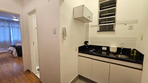 A compact kitchen with a black countertop, white cabinets, and a small window with blinds. - Copacabana Breeze Studio, 5 minutes from the beach (Rio de Janeiro)