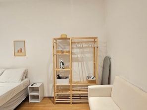 A room with a bed, a wooden wardrobe with shelves, a small table, and a painting on the wall. - Copacabana Breeze Studio, 5 minutes from the beach (Rio de Janeiro)