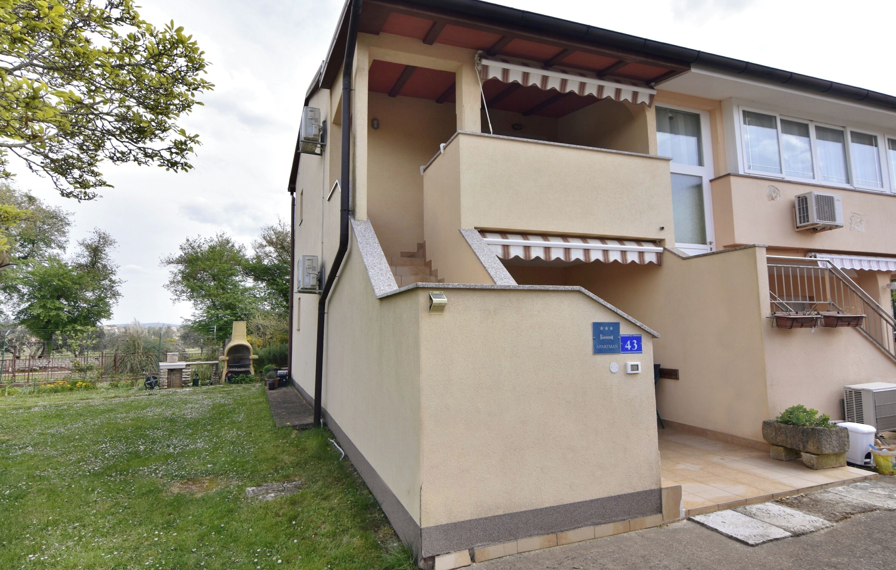 A two-story building with a flat roof, a staircase leading to the upper floor, and a small outdoor area with a grill.