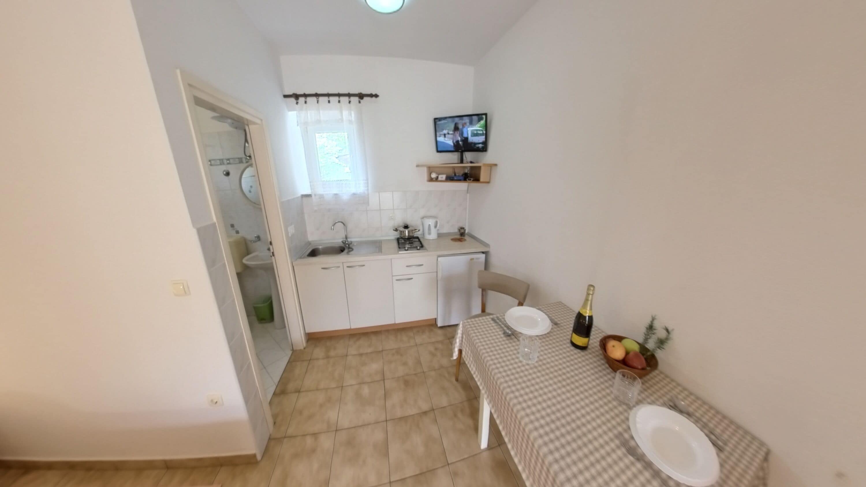 A compact kitchen with a sink, stove, and a television mounted on the wall.