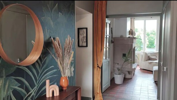 A hallway with a mirror, a vase with dried plants, and a framed picture on a wall. - Villa Bénédictins (Limoges)