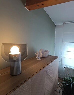 Une chambre moderne avec un bureau en bois, un luminaire fixé au mur, un objet décoratif en forme de corail et une plante en pot.