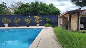 A swimming pool with a tiled deck, surrounded by potted plants and a small building with a tiled roof. - Villa Bénédictins (Limoges)