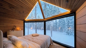 A cozy bedroom with a large window, a bed, a bedside table with a lamp, and a deer's head decoration.