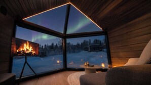 A cozy room with a fireplace, a couch, and a view of the snowy landscape and aurora.