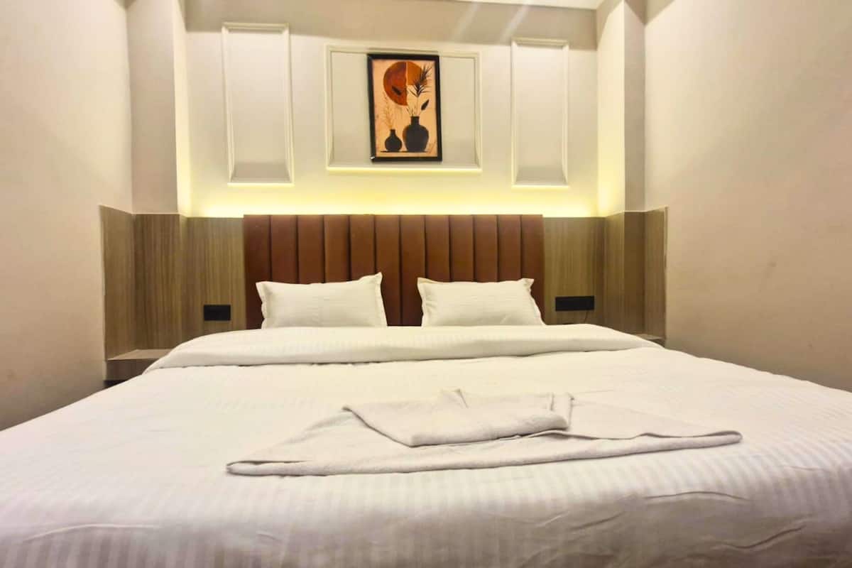 Habitación de hotel con una cama grande, dos almohadas, cabecera con panel de luz y una obra de arte enmarcada sobre la cama.