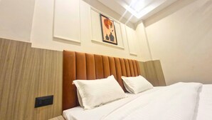 A hotel room with a bed, a headboard, a wall-mounted light, and a framed picture. - The City Hotel (Kanpur)