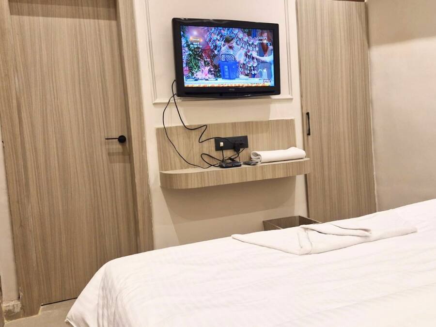 Une chambre d’hôtel avec un lit, un téléviseur fixé au mur, une étagère avec une serviette et une porte.