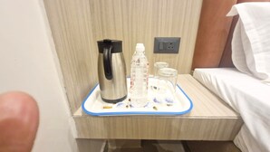 A hotel room with a bed, a nightstand, a tray with a water bottle, a glass, and a kettle. - The City Hotel (Kanpur)