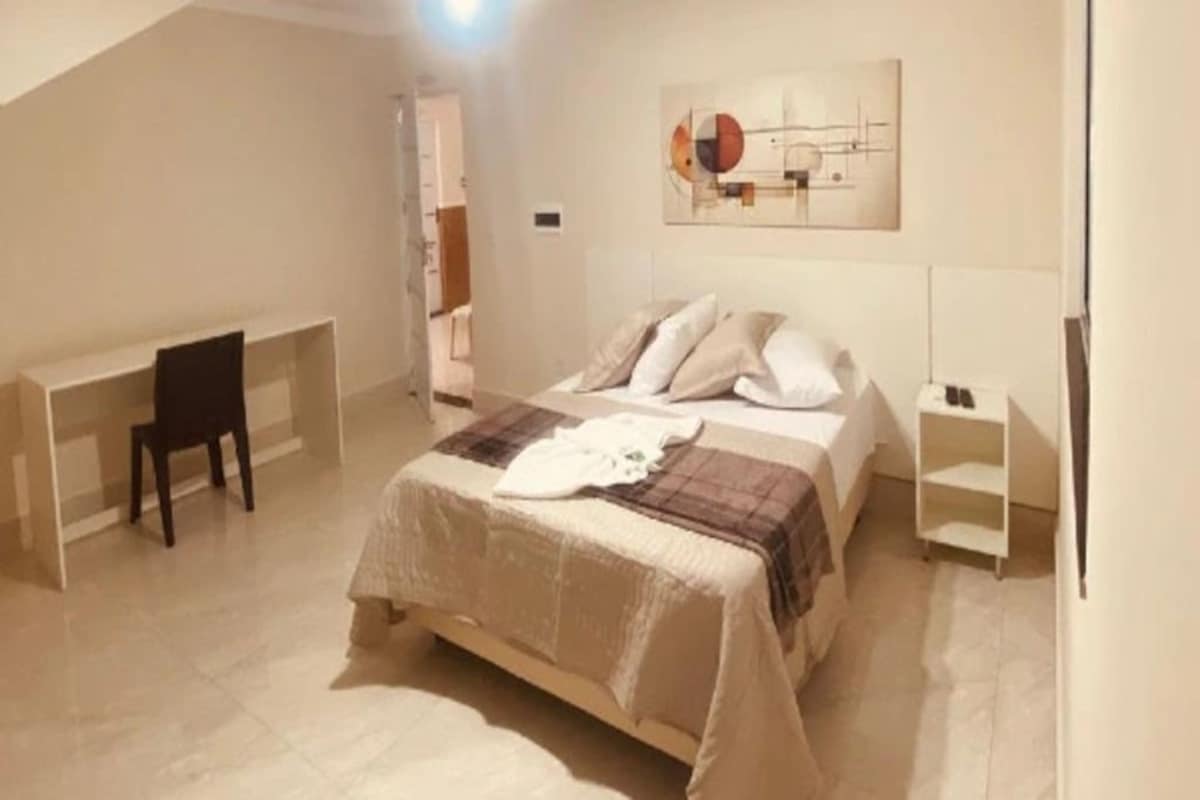 A bedroom with a bed, a desk, and a chair. There is a painting on the wall.