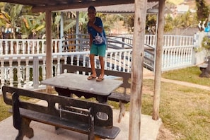 A picnic table and bench under a shelter with a white fence in the background. - Pousada Chácara Santa Inês (Conceição do Mato Dentro)