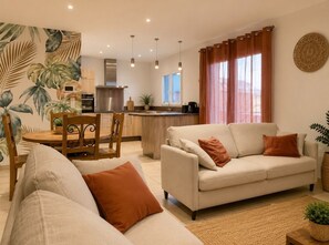 Ein Wohnzimmer mit einer Couch, einem Esstisch mit Stühlen, einer Küchenzeile und einem großen Fenster mit Vorhängen.