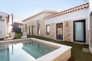 Un área junto a la piscina con un edificio de piedra, una piscina pequeña y dos sillones de descanso.