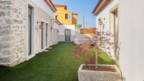 Un patio con muros de piedra, césped verde y un edificio amarillo al fondo.