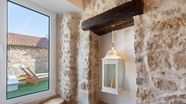 Una habitación de paredes de piedra con una ventana, un banco de madera y un farol colgante.