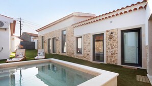 Un área junto a la piscina con un edificio de piedra, una piscina pequeña y dos sillones de descanso.