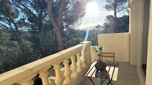 Un balcón con vistas a árboles, una planta en maceta y un banco de madera.