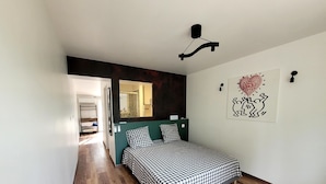 Un dormitorio con cama, suelo de madera, un espejo y decoración en la pared.