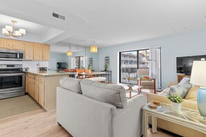 Eine moderne Küche mit Einbauofen, ein Essbereich mit Tisch und Stühlen, ein Wohnzimmer mit Sofa und Fernseher sowie ein Balkon mit Aussicht.