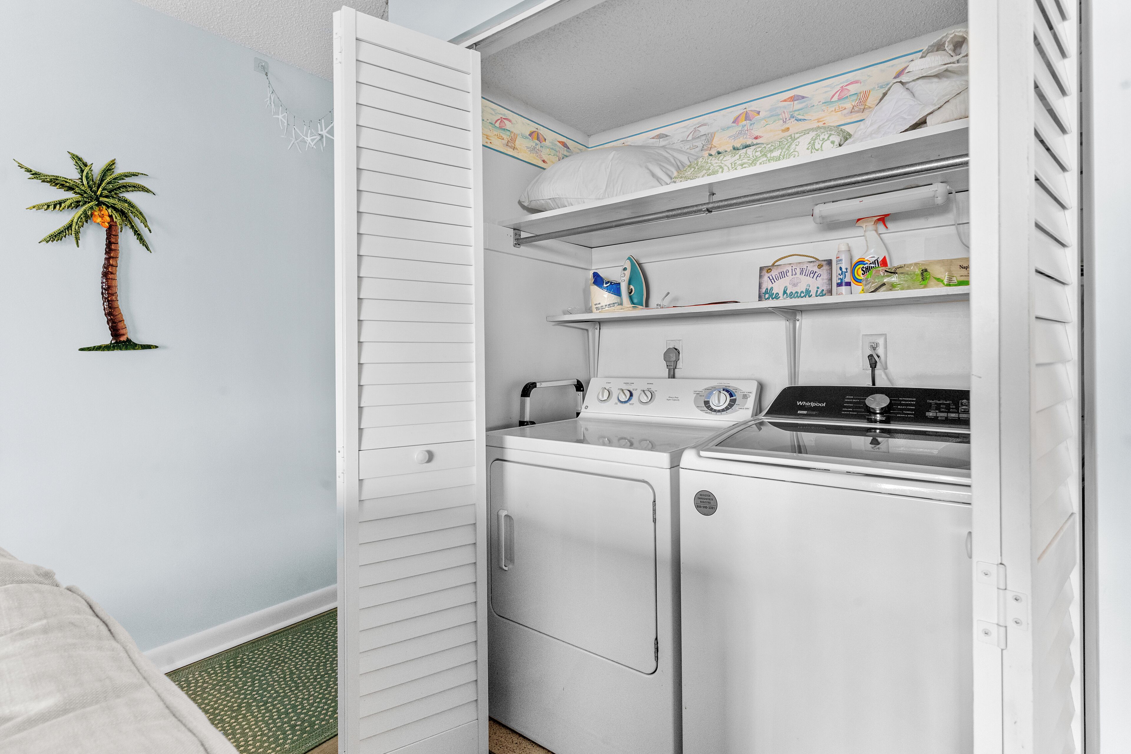 Un cuarto de lavandería con lavadora, secadora y repisas superiores con productos de limpieza.