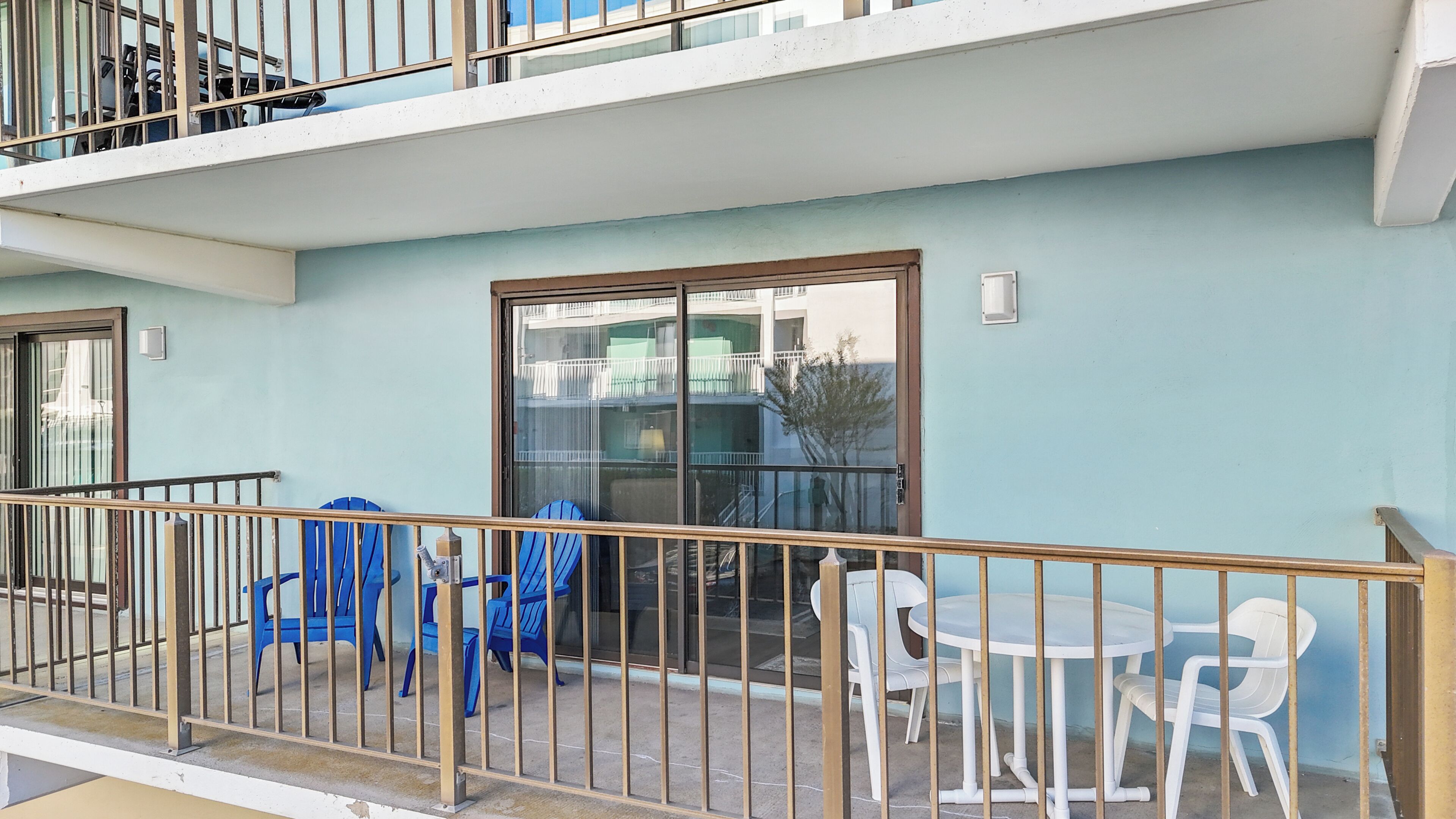 A balcony with blue and white plastic chairs, a small round table, and a glass door leading to an interior space.