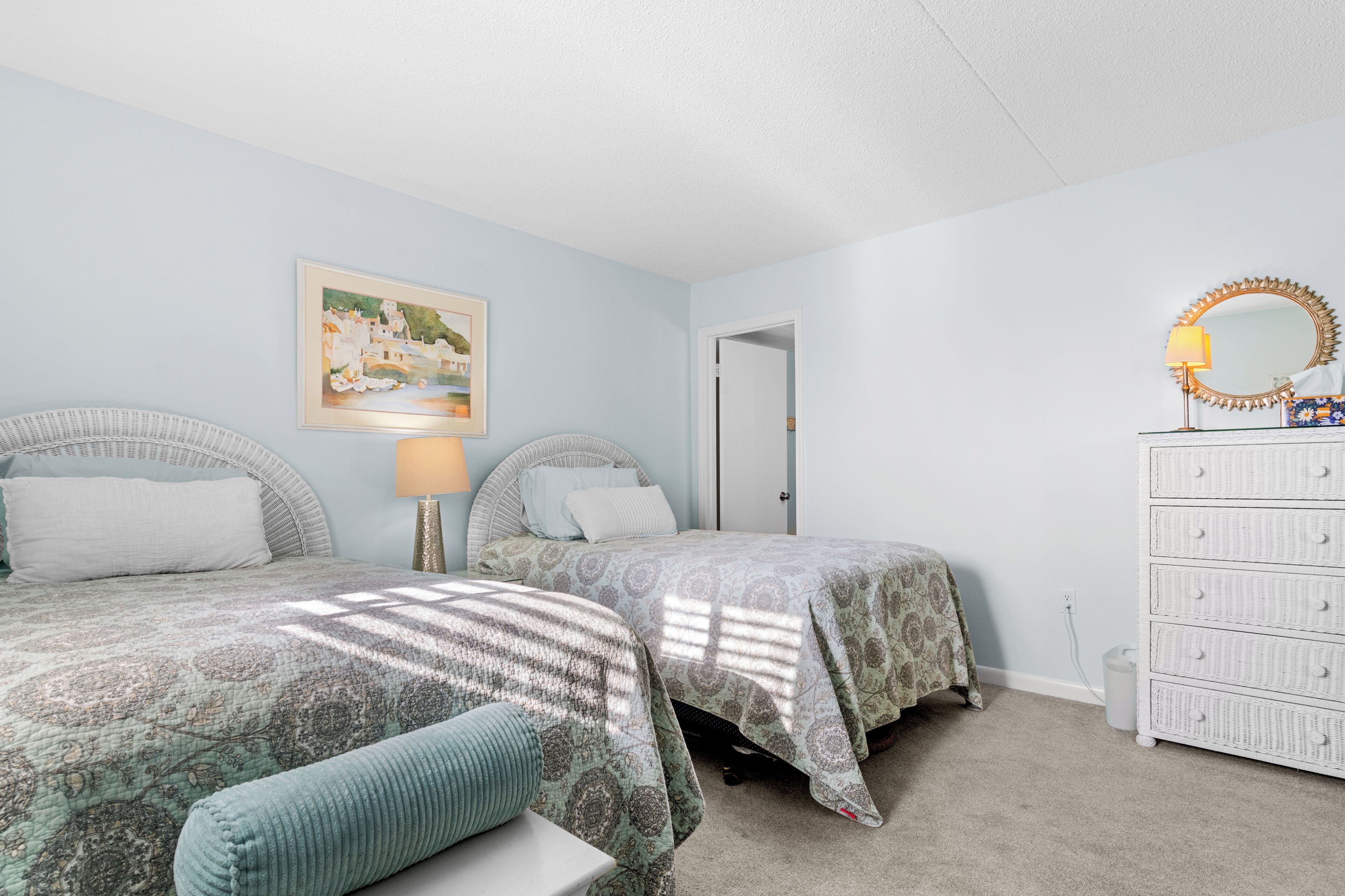 A bedroom with two beds, a dresser, a lamp, and a painting on the wall.