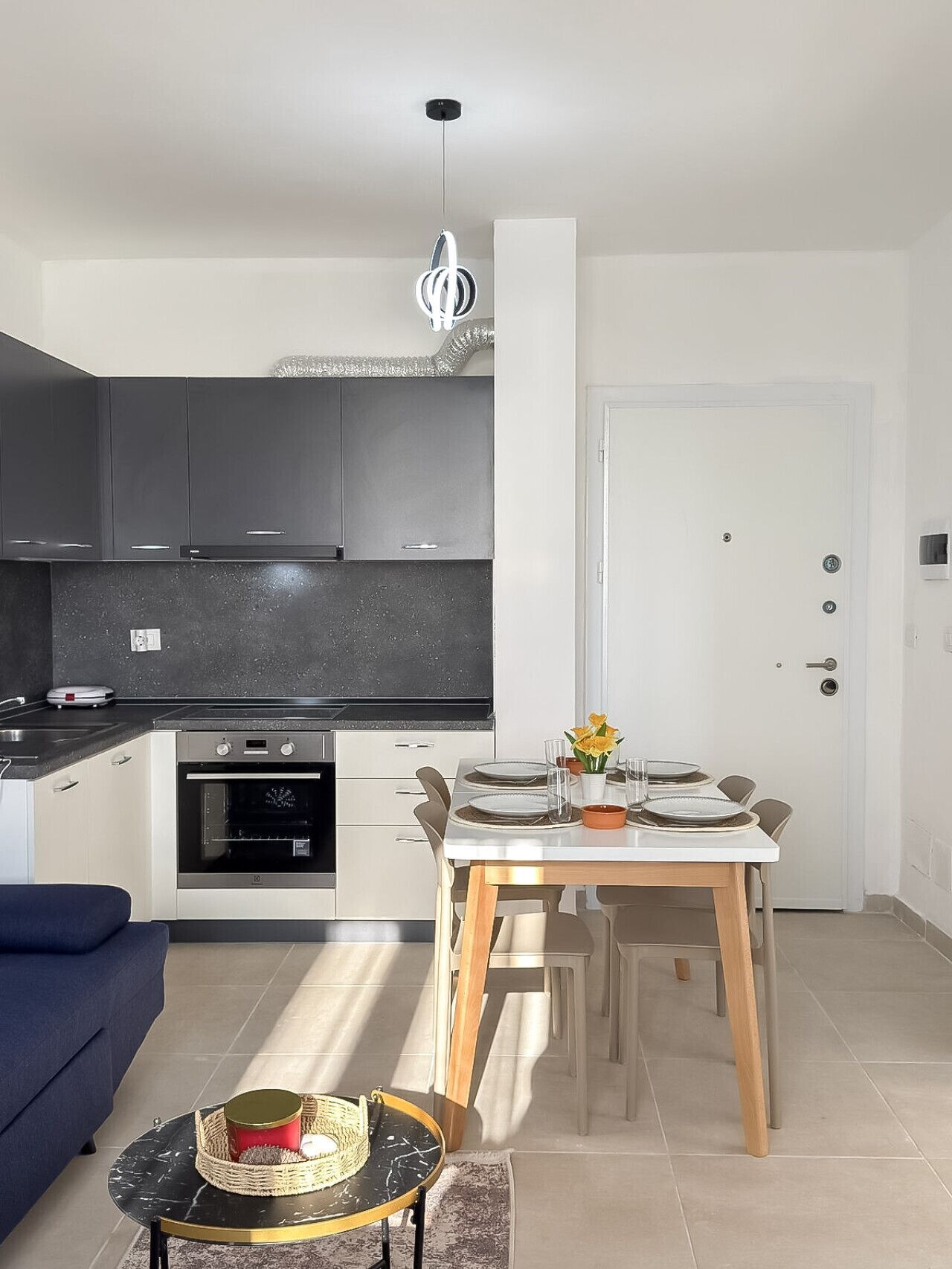 Una cucina moderna con mobili scuri, un tavolo da pranzo per quattro persone e un divano blu nella zona living.