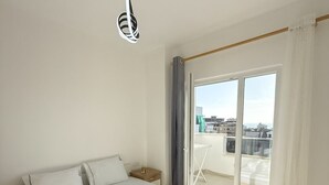 A modern hotel room with a large bed, a view of the city through the balcony, and a hanging light fixture.