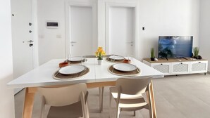 A modern dining area with a white table set for four, a television on a white cabinet, and a door with a lock.